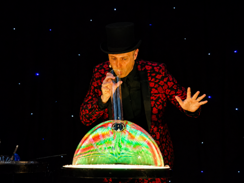 Allan Hart réalisant une grande bulle de savon aux couleurs irisées sur scène